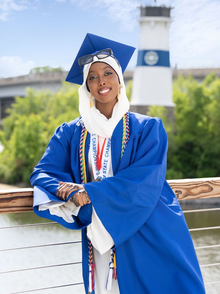 Graduate in a blue gown and white hijab by the river