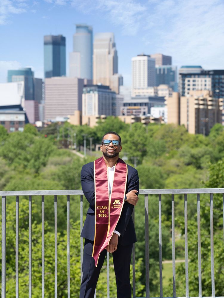 Graduate in a suit and stole with the Minneapolis skyline