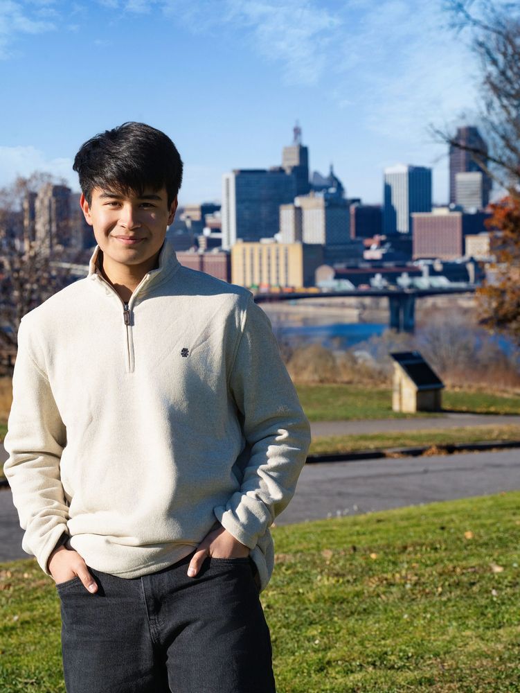 Young man in a cream sweater with a city skyline behind